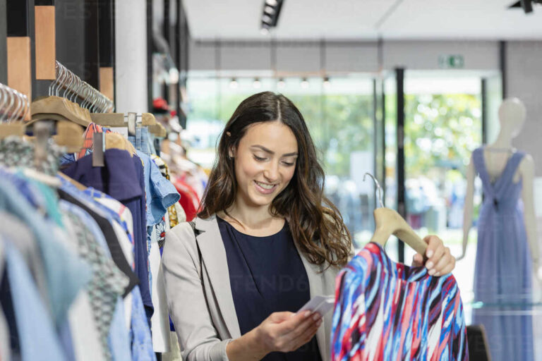 young-woman-looking-at-price-tag-while-holding-dress-in-boutique-EIF01534